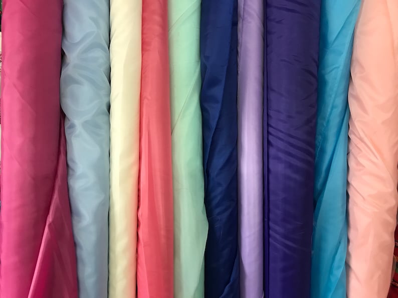 May include: A collection of fabric rolls in various colors, including pink, blue, light blue, cream, mint green, purple, navy blue, turquoise, and peach.