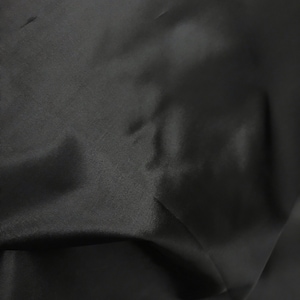 May include: Close-up of a black fabric with a smooth, slightly shiny texture. The fabric is wrinkled and folded, showing its drape and flexibility.