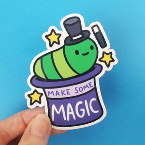 May include: A green worm wearing a purple top hat with a black wand and yellow stars. The hat says "Make Some Magic".
