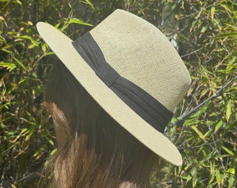 May include: A light beige fedora hat with a black band. The hat has a classic, structured design with a wide brim. The hat is made of a woven material, perfect for sun protection. The hat is a stylish accessory.
