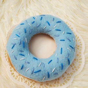 May include: A blue felt donut with white and blue sprinkles. The donut is on a white doily.