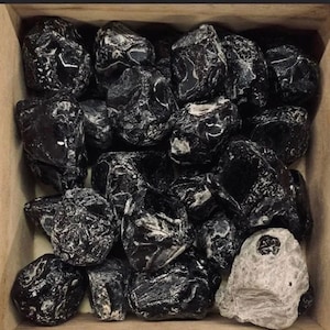 May include: A collection of black obsidian tumbled stones in a wooden box. The stones are smooth and have a shiny, almost glassy finish.