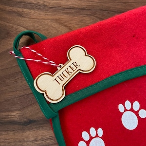 May include: Red and green Christmas stocking with white paw prints and a wooden bone-shaped tag that says "Tucker".