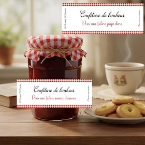 Peut inclure: Un pot de confiture rouge avec un couvercle à carreaux rouges et blancs, attaché avec de la ficelle. Le pot porte une étiquette avec l'inscription "Confiture de bonheur" et "Pour une future mamie d'amour". Une tasse de thé et des biscuits sont en arrière-plan.