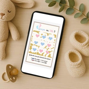 May include: A smartphone displays a gender reveal game with blue and pink hearts. The text "Garçon ou Fille?" is at the top. A plush bunny, pacifier, and baby booties are also in the image.
