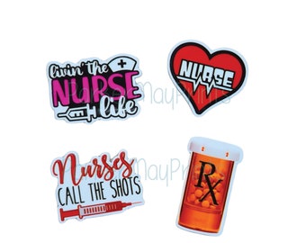 May include: Four colorful stickers with nurse-themed designs. The first sticker is white with pink and black text that reads "Livin' the Nurse Life" with a small red cross and a syringe. The second sticker is a red heart with white text that reads "Nurse" and a white EKG line. The third sticker is white with red text that reads "Nurses Call the Shots" with a red syringe. The fourth sticker is a white pill bottle with a red cap and a black "Rx" and orange pills inside.