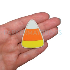 May include: A white, orange, and yellow candy corn cutout. The candy corn is in the shape of a triangle with rounded edges.