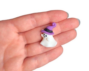 May include: A white ghost with a purple witch hat and black eyes. The ghost is holding a small, white wand.