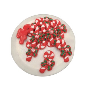 May include: A collection of red and white candy canes with green bows and snowflake accents, arranged on a white circular surface. The candy canes are a festive holiday decoration.