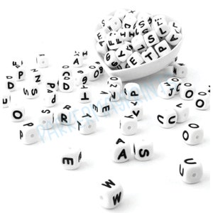 May include: White alphabet letter beads with black lettering. The beads are scattered on a white surface and some are in a white bowl.