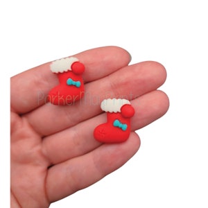 May include: Two red Christmas stocking charms with white fur trim, blue bows, and a red pom-pom on top.