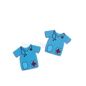 May include: Two light blue scrubs-style shirt charms with a stethoscope, a red heart, and a red cross. The charms have a pocket design and are set against a white background. These charms are ideal for medical-themed crafts.