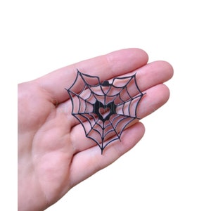 May include: Black spiderweb cutout with a heart in the center. The web is in the shape of a heart.