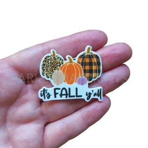 May include: A white sticker with the text "it's FALL y'all" and four pumpkins. The pumpkins are decorated with leopard print, buffalo plaid, and solid orange and purple.