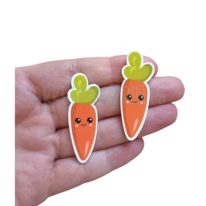 May include: Two orange carrot stickers with green tops and happy faces.