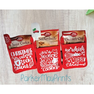 May include: Three red oven mitts with white text and designs. The mitts are decorated with Christmas-themed sayings, including "Christmas calories don't count", "Tis the season for baking cookies", and "We whisk you a Merry Christmas".