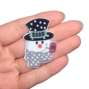 May include: A snowman with a black and white polka dot hat, green and white striped band, and a gray and white polka dot scarf. The snowman is holding a red pipe.