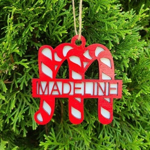 May include: Red and white candy cane ornament with the name Madeline cut out in the center.