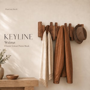 May include: A wall-mounted walnut wood piano rack labeled KEYLINE Walnut Classic Linear Piano Rack and PineCone No.01. The rack features multiple vertical slats that fold down as hooks, currently holding a beige scarf, a brown jacket, and a brown hat.
