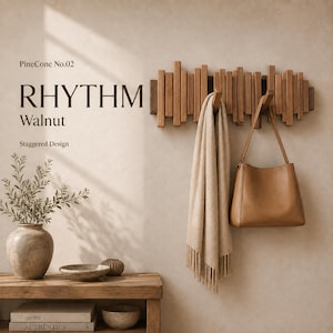 May include: A wall-mounted walnut coat rack with a staggered vertical slat design. The text on the wall reads PineCone No.02, RHYTHM, Walnut, and Staggered Design. A beige scarf and a tan leather handbag hang from the wooden hooks on the rack.