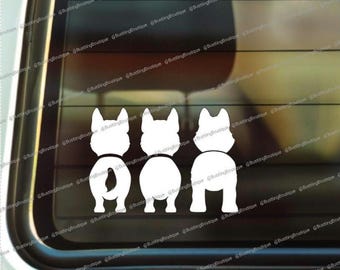 May include: A white vinyl decal featuring three stylized dog silhouettes, viewed from the rear. The dogs are depicted with their tails and hindquarters visible, creating a playful and whimsical design. Ideal for car windows.