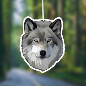 May include: A gray wolf head with yellow eyes, a black nose, and a white muzzle. The wolf is looking directly at the viewer. The image is a car air freshener.