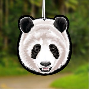 May include: A panda bear face air freshener with a black outline, black ears, and black patches around the eyes. The panda has a white face and a smiling mouth. A white string is attached for hanging.