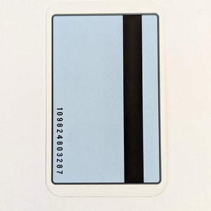 K&ouml;nnte beinhalten: Eine rechteckige Karte mit hellblauem Hintergrund und einem schwarzen Magnetstreifen auf der rechten Seite. Die Karte hat abgerundete Ecken und einen wei&szlig;en Rand. Die Nummer "109824803287" ist vertikal auf der linken Seite aufgedruckt.