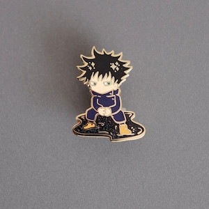 Pode incluir: Um broche de esmalte dourado com um personagem de desenho animado com cabelo preto, camisa azul e botas amarelas. O personagem est&aacute; sentado em uma po&ccedil;a preta e dourada.