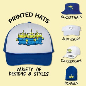 May include: A variety of printed hats featuring a group of three green alien characters. The hats include bucket hats, sun visors, trucker caps, and beanies. The text "PRINTED HATS" is at the top of the image.