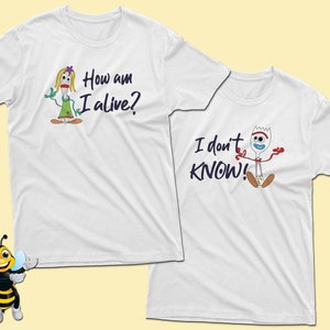 May include: Two white t-shirts with a cartoon image and text. The first shirt features a cartoon image of a female character with the text "How am I alive?" The second shirt features a cartoon image of a male character with the text "I don't KNOW!"