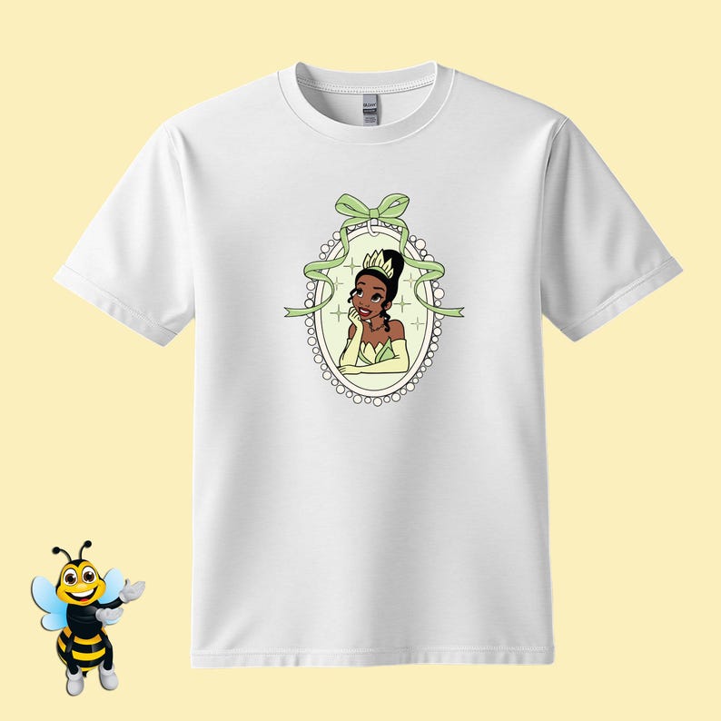 Puede incluir: Camiseta blanca con una ilustraci&oacute;n de dibujos animados de una princesa con un vestido y corona verdes, enmarcada por una cinta verde y un borde de perlas. El dise&ntilde;o est&aacute; centrado en la camiseta, ofreciendo una est&eacute;tica caprichosa y colorida.