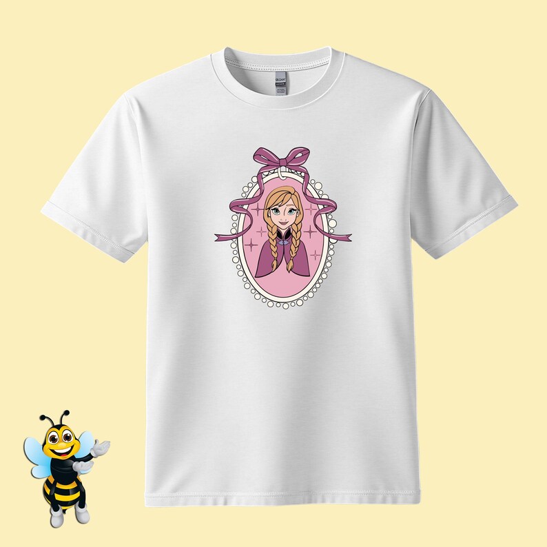 Puede incluir: Camiseta blanca con una ilustraci&oacute;n de dibujos animados de un personaje con trenzas rubias, que lleva una capa morada, dentro de un marco ovalado rosa con un lazo y una cinta. El dise&ntilde;o est&aacute; centrado en la camiseta.