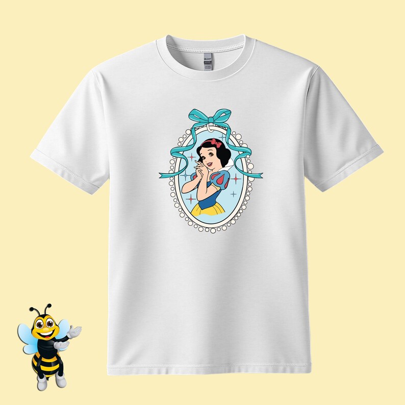 Puede incluir: Camiseta blanca con una imagen de dibujos animados de Blancanieves en un marco ovalado azul y blanco con un lazo azul. La imagen de Blancanieves tiene un bob negro, un lazo rojo y un vestido azul y amarillo.