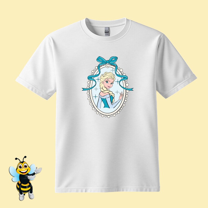 Puede incluir: Camiseta blanca con una ilustraci&oacute;n de dibujos animados de una mujer rubia con un vestido azul, enmarcada por un &oacute;valo con un lazo y una cinta azules. El dise&ntilde;o est&aacute; centrado en la parte delantera de la camiseta.