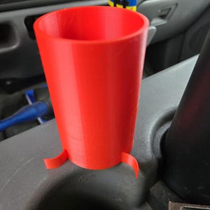 以下が含まれることがあります： 車両のカップホルダー用に設計された、鮮やかな赤色の3Dプリントカップホルダー。 カップホルダーは円筒形で、上部がフレアになっており、安定性を高めるためにベースに3つの小さなタブが付いています。 内側は中空です。