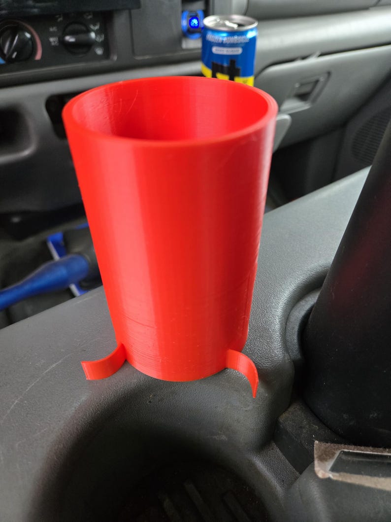 以下が含まれることがあります： 車両のカップホルダー用に設計された、鮮やかな赤色の3Dプリントカップホルダー。 カップホルダーは円筒形で、上部がフレアになっており、安定性を高めるためにベースに3つの小さなタブが付いています。 内側は中空です。