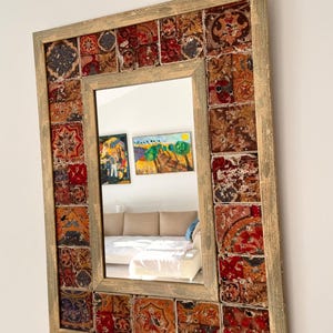 May include: A rectangular wall mirror featuring a frame decorated with a mosaic of square tiles in shades of red, orange, brown, and blue. The tiles display intricate, weathered patterns, and the frame is finished in a light, distressed wood tone.
