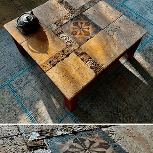 Könnte beinhalten: Quadratischer Couchtisch mit Mosaikfliesen. Der Tisch hat ein zentrales Blumendesign und besteht aus Stein und Holz. Eine schwarze Teekanne steht auf der Tischoberfläche. Der Tisch steht auf einem gemusterten Teppich.