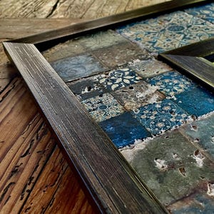 Könnte beinhalten: Nahaufnahme eines dunkelbraunen Holzrahmens mit einem Mosaik aus blauen und weißen Fliesen. Die Fliesen sind in einem zufälligen Muster angeordnet und haben einen abgenutzten Look. Der Rahmen befindet sich auf einer Holzoberfläche.