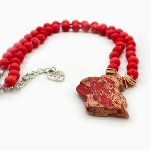 May include: Red lava rock bead necklace with a red and gold jasper pendant and a silver charm that says "made with love".