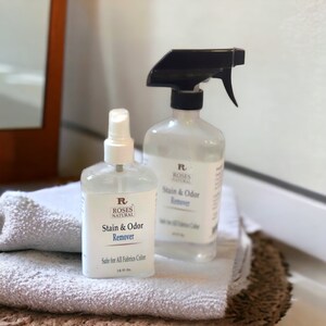May include: Two clear spray bottles with white labels and black trigger sprayers. The labels read "Roses Natural Stain & Odor Remover". The smaller bottle says "Safe for All Fabrics Colour 1.6 fl oz".