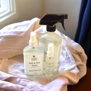 May include: Three clear spray bottles with white labels. The largest bottle has a black spray nozzle and the label reads "Roses Natural Stain & Odour Remover". The smallest bottle has a white spray nozzle and the label reads "Safe for All Fabrics Colours".