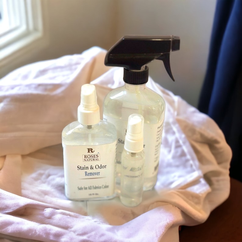 May include: Three clear spray bottles with white labels. The largest bottle has a black spray nozzle and the label reads "Roses Natural Stain & Odour Remover". The smallest bottle has a white spray nozzle and the label reads "Safe for All Fabrics Colours".