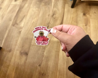 May include: A sticker featuring a green puppet wearing a pink dress and holding a wand. The sticker has the text "Who's that wonderful girl? Could she be any cuter?"