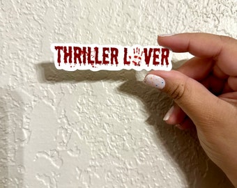 May include: A white sticker with the words "THRILLER LOVER" in red dripping letters. The letters are stylized to look like blood dripping.