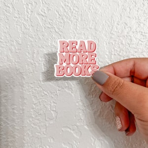 Può includere: Sticker rosa e rosso con il testo "READ MORE BOOKS" in uno stile di font retrò.