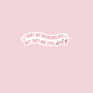 May include: Pink sticker with the text "I dust my bookshelves but they are still dirty" in a white outline with pink stars on either side.