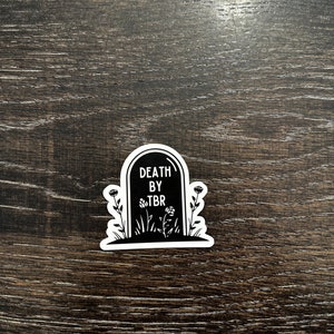 May include: Black and white sticker of a tombstone with the text "DEATH BY TBR" and flowers.