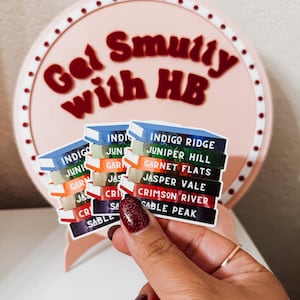 May include: A stack of colorful book-shaped stickers with the names of different places, including Indigo Ridge, Juniper Hill, Garnet Flats, Jasper Vale, Crimson River, and Sable Peak.